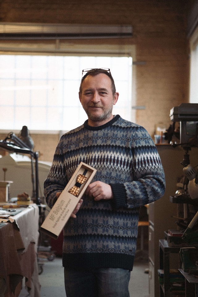 User standing with his wooden bow ties in his workshop